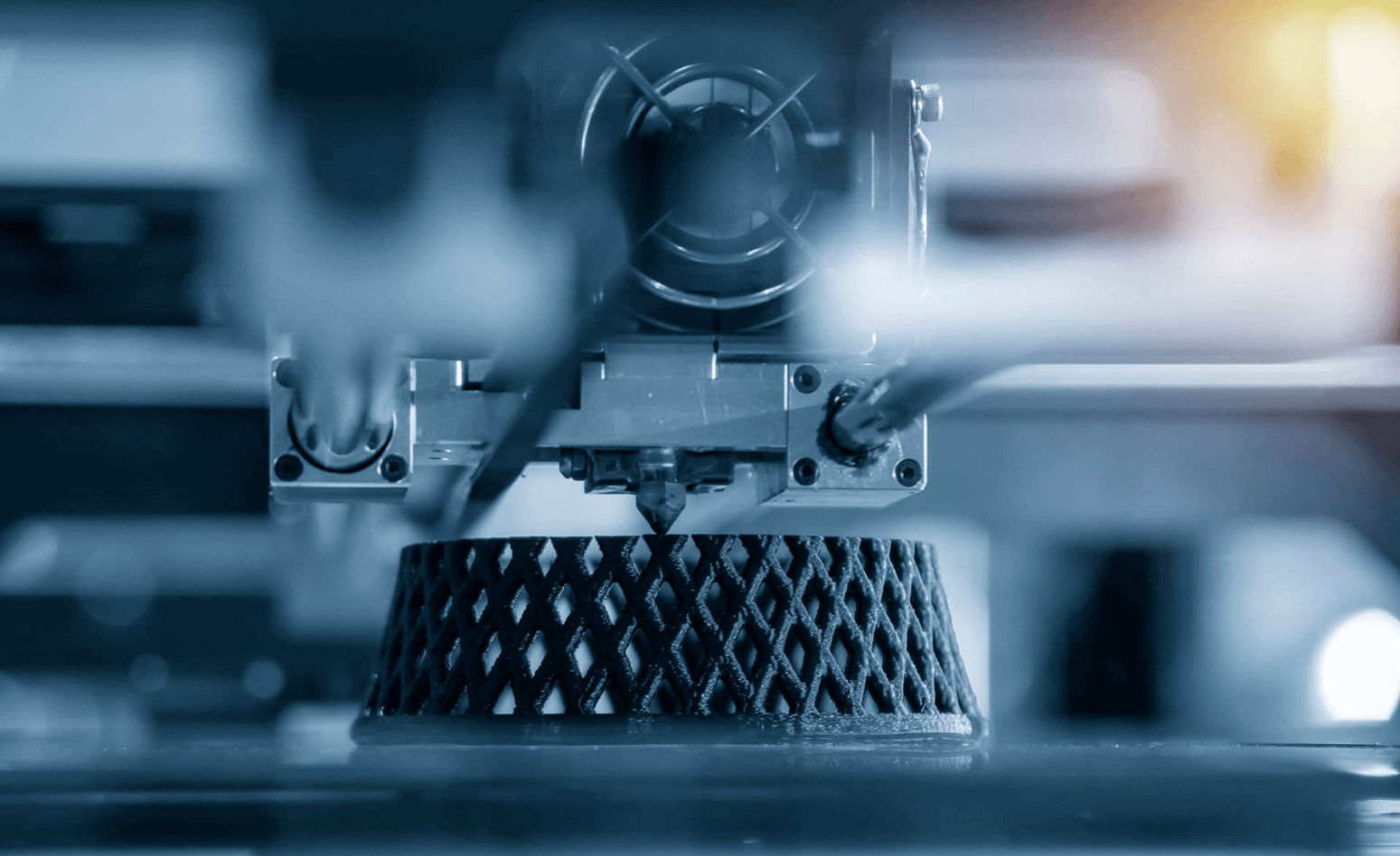 Bild einer 3D-Druckerdüse, die Kunststoff auf eine gitterförmige Unterlage extrudiert und damit die fortschrittliche Technologie der additiven Fertigung demonstriert.